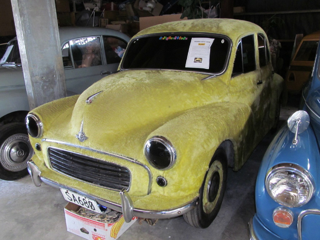 Mehrere Oldtimer stehen vor einer Wand mit verschiedenen Accessoires, wobei auf der linken Seite eine Säule zu sehen ist.