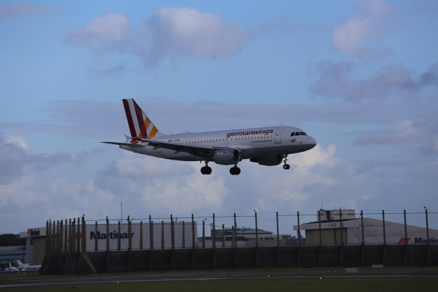 Germanwings Airbus A320-200 startet von Frankfurt Airport, mit Gras darunter, einem Zaun im Vordergrund, Gebäuden und Bäumen im Hintergrund und einer bewölkten Himmel