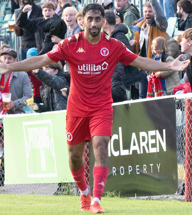 Ein Fussballspieler in roter Uniform rennt mit ausgestreckten Armen auf einem Feld, mit einer Menge im Hintergrund und einem Banner mit der Aufschrift "Middlesbrough FC v Swansea City - Sky Bet Championship" im Vordergrund.