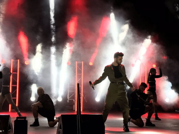 Drake performs auf der Bühne beim Coachella Valley Music and Arts Festival 2018, ein Mikrofon haltend, umgeben von tanzenden Menschen in einer Hockposition, mit Lautsprechern, einer Kameramann, Metallstangen und einer Decke mit Deckenleuchten.