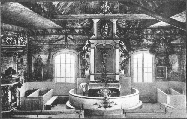 Schwarzes und wei├čes Foto einer Kirche mit einem zentralen Brunnen, flankierenden B├Ąnken, Fenstern im Hintergrund und skulpturalen Wandschmuck, mit Text unten.