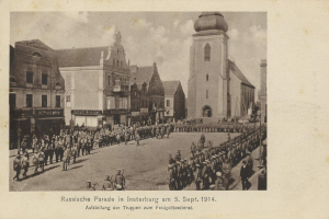 Ein Schwarz-Weiß-Foto eines Umzugs in Insterburg am 5. September 1914, das viele Menschen zeigt, einige stehen und einige gehen, mit Gebäuden im Hintergrund und Text unten auf dem Bild.