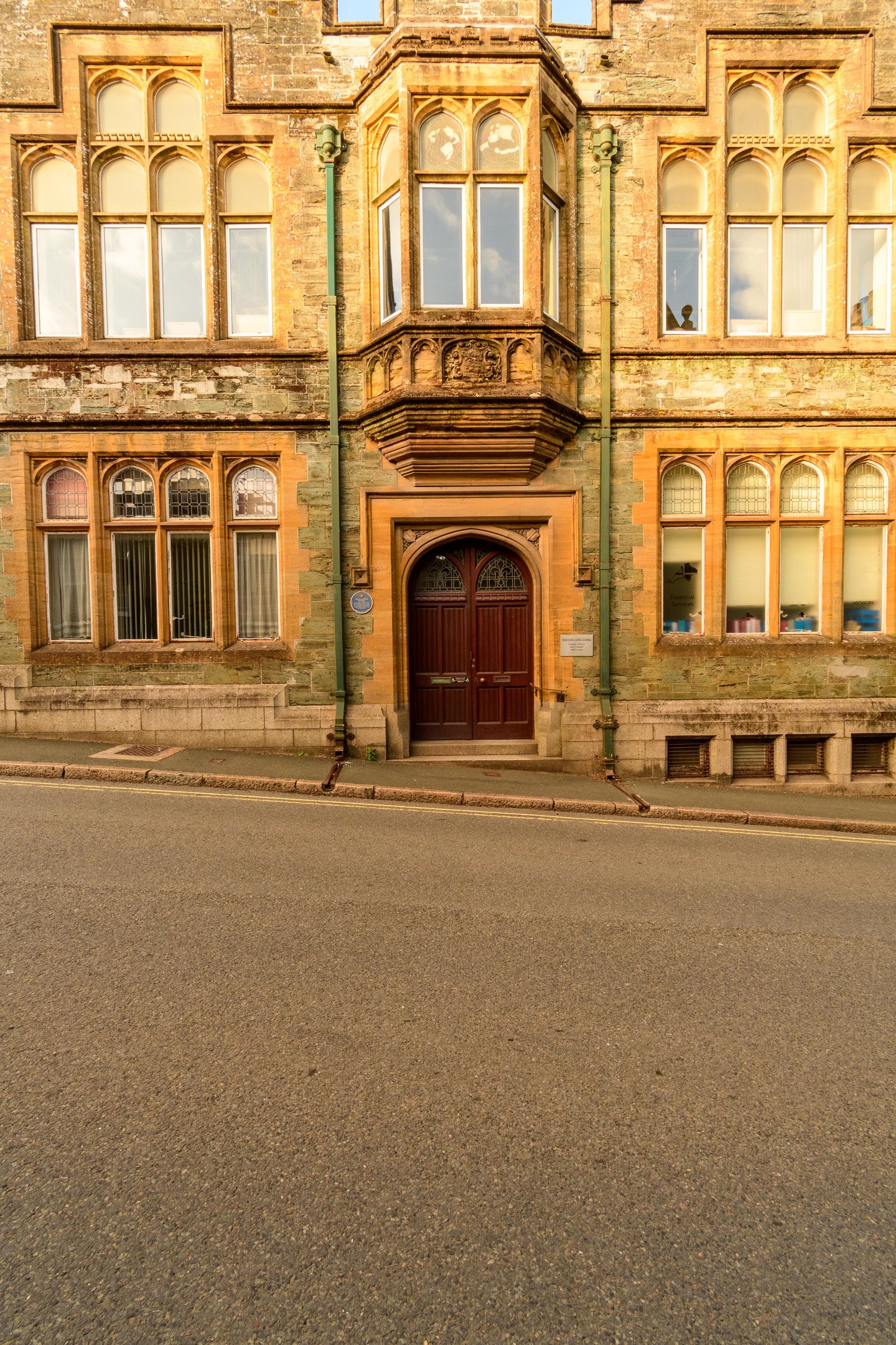 Altes Gebäude mit zahlreichen Fenstern, einer Holztür und sichtbaren Rohren an seinen Außenwänden, das neben einer Straße steht.