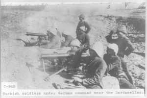 Schwarzes und weißes Foto von türkischen Soldaten unter deutschem Kommando in der Nähe der Dardanellen, die Helme tragen und Waffen halten, mit Text unten.