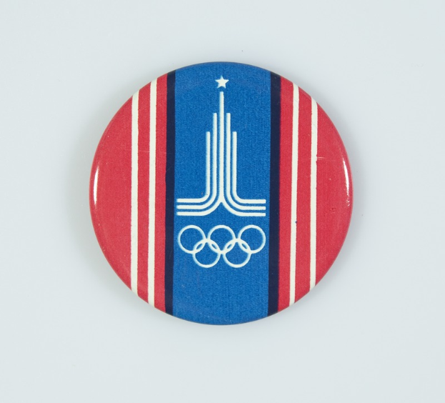 Ein rundes Abzeichen mit einem blauen und weißen Design, das die ikonischen Olympischen Ringe in der Mitte zeigt, vor einem weißen Hintergrund.