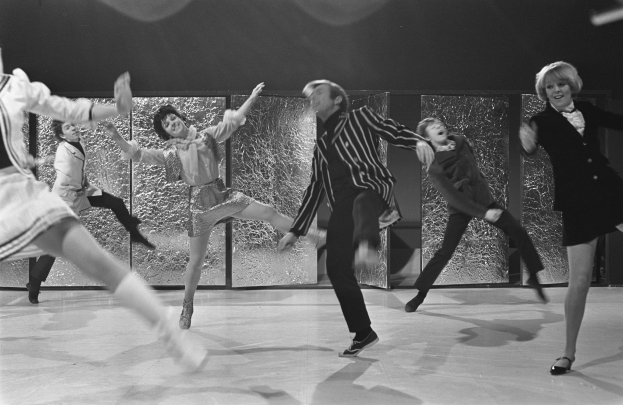 Eine Gruppe von Menschen, die auf einer Bühne tanzen, in Schwarz-Weiß, mit Schuhen, mit einer Wand im Hintergrund.
