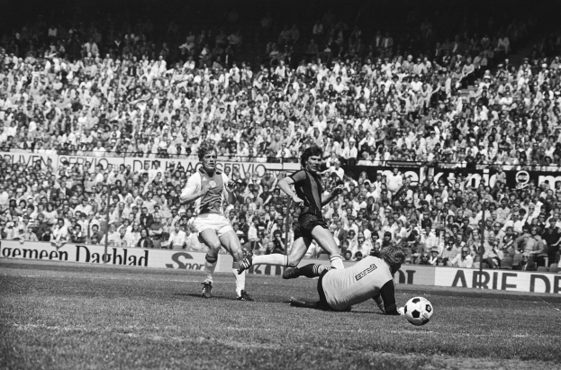 Schwarzes und weißes Foto von Fussballspielern im Einsatz auf einem Feld mit Zuschauern im Hintergrund und einer Bundesliga 1978-79 Ajax 1-1 Hannover 96 Fahne.