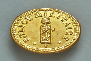 Eine Goldm├╝nze mit der Aufschrift "Police Militaire" vor einem weißen Hintergrund.