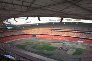 Großes Stadion voller Zuschauer, Fahrzeuge auf der Straße, grasbewachsener Boden, Texttafeln, Geländer, ein Bildschirm und Deckenbeleuchtung.