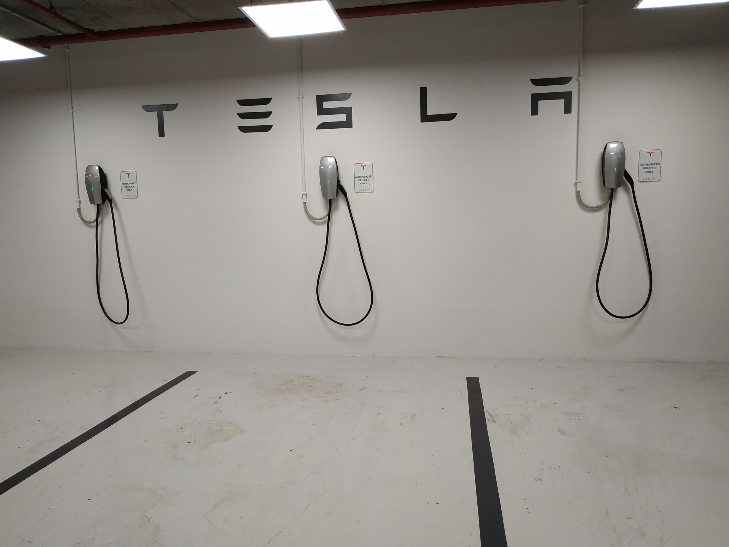 Eine Tesla-Ladestation in einer Tiefgarage mit angeschlossenen Kabeln und Deckenbeleuchtung, die die darunterliegende Etage zeigt.
