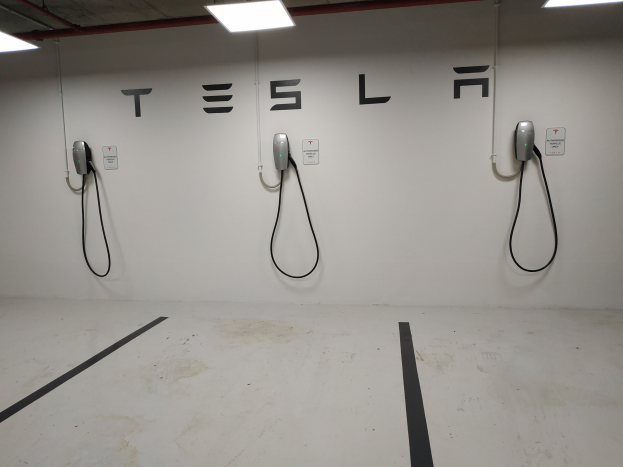 Eine Tesla-Ladestation in einer Tiefgarage mit angeschlossenen Kabeln und Deckenbeleuchtung, die die darunterliegende Etage zeigt.