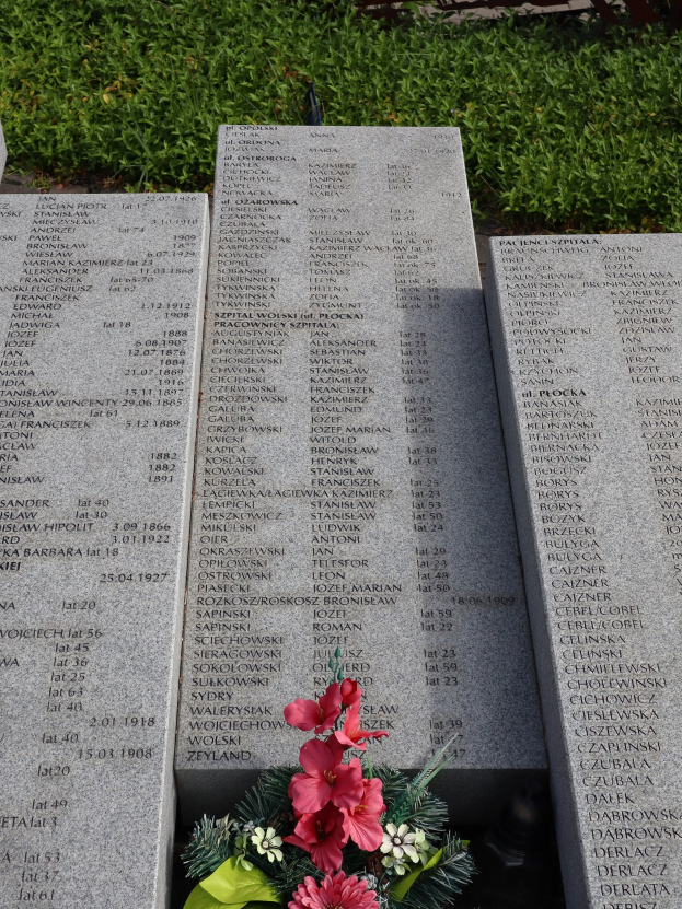 Gedenkstein mit einem Blumenstrauß darauf, umgeben von grünem Gras, mit Text, der wahrscheinlich Kriegstote ehrt.