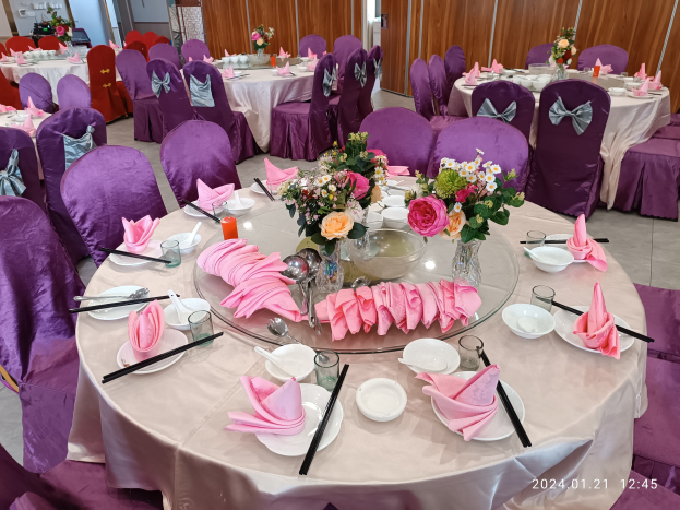 Festlich gedeckte Tafel mit Stühlen für ein Event, mit Gedecken, Servietten, Blumenvasen und einer Wand im Hintergrund.
