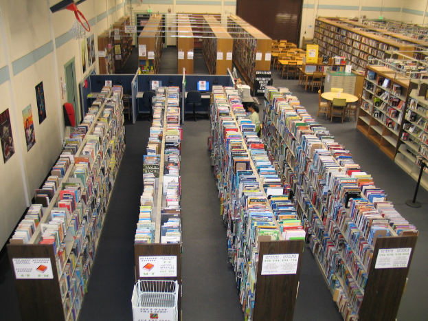Eine Bibliothek mit Bücherregalen voller Bücher und Tischen und Stühlen vor einer Wand.