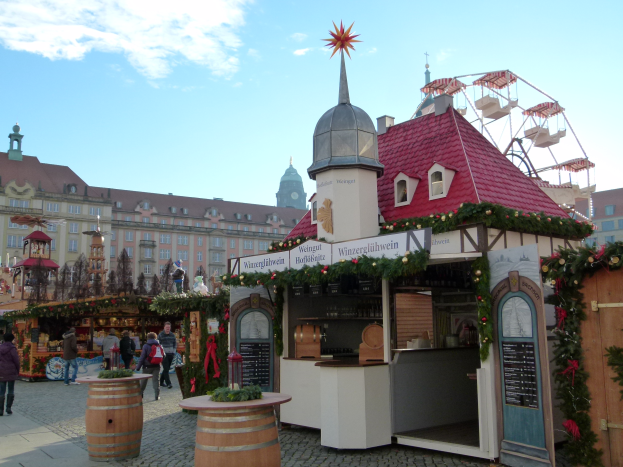 Ein lebendiger Weihnachtsmarkt in Nürnberg, Deutschland, mit Menschen um dekorierte Stände, Gebäude, ein Riesenrad und eine Tafel auf der rechten Seite.
