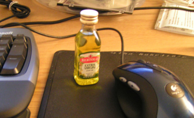 Ein Tisch mit verschiedenen Gegenständen, darunter Kabel, eine Maus, eine Tastatur, eine Scheibe, Notizen, eine Flasche mit Flüssigkeit und eine Mausauflage.