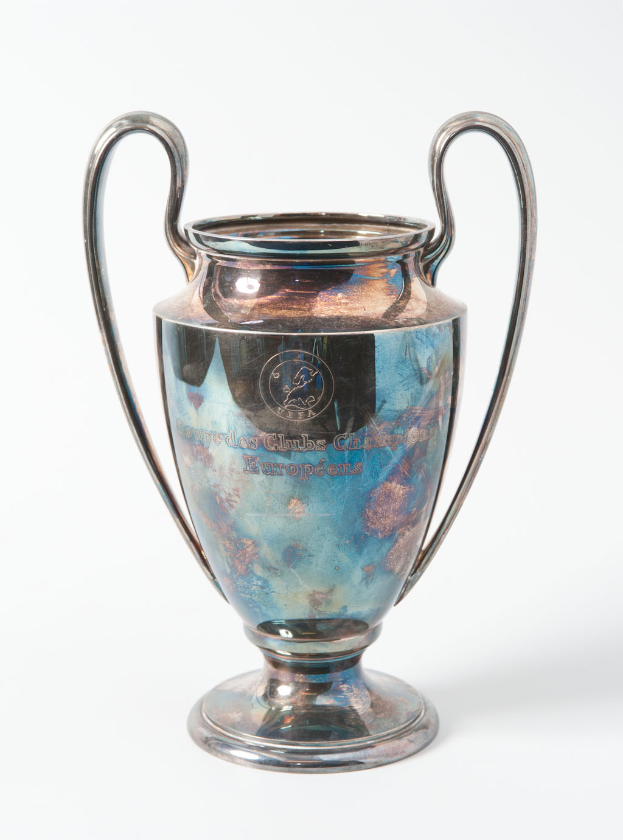 Der UEFA-Champions-League-Pokal, ein stählerner Becher mit zwei Griffen und einem blauen und silbernen Farbschema, mit der Inschrift «UEFA Champions League» auf einem weißen Hintergrund.