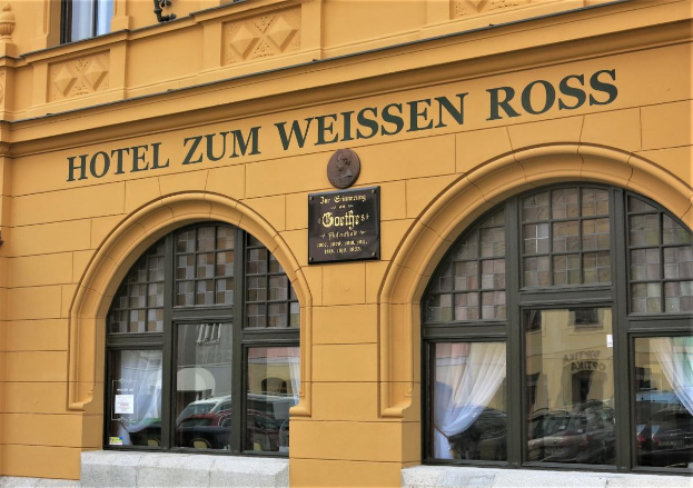Das Hotel Zum Weissen Ross in Wien, Österreich, ein Gebäude mit Glasfenstern und -türen, ein Schild mit Text und eine Straße davor.