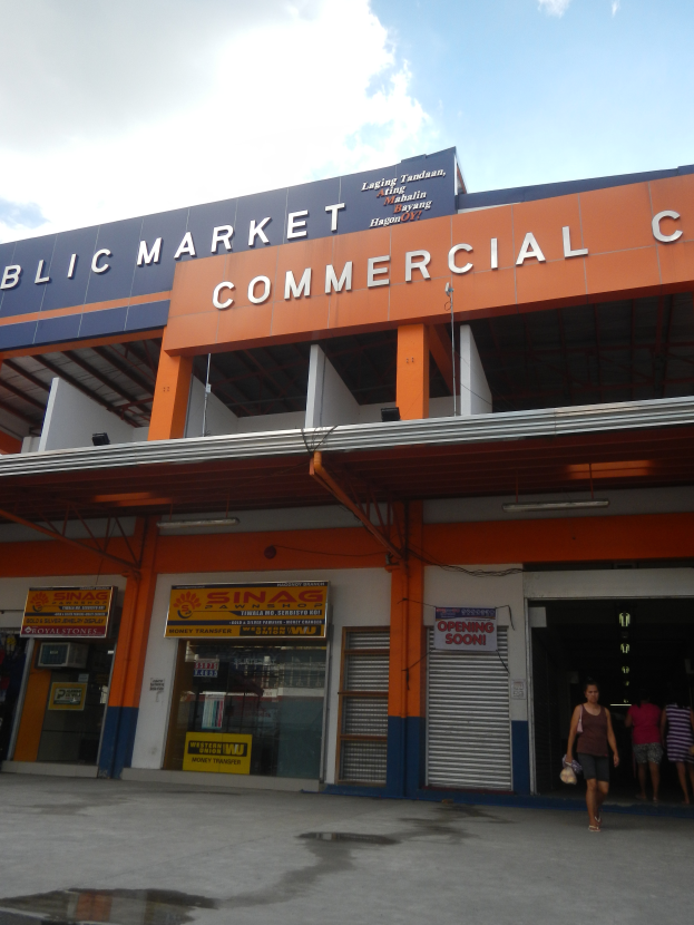 Ein öffentlicher Markt mit Menschen davor, Text an dem Gebäude und ein sichtbarer Himmel oben.