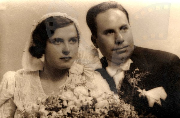 Schwarz-weißes Foto eines lachenden Mannes und einer Frau an ihrem Hochzeitstag, die Frau in einem weißen Kleid mit einem Strauß Blumen in der Hand, der Mann steht neben ihr.