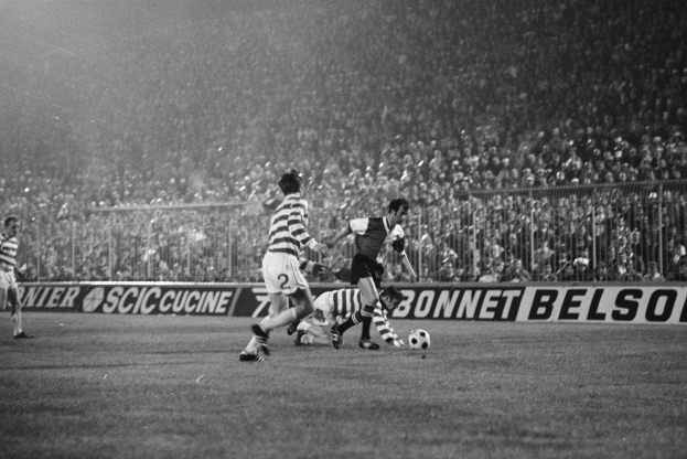 Ein Schwarz-Weiß-Bild einer Gruppe von Männern, die auf einem Feld Fußball spielen, mit Zuschauern auf den Rängen und einem Banner mit der Aufschrift "Celtic v West Bromwich Albion - FA Cup Third Round."