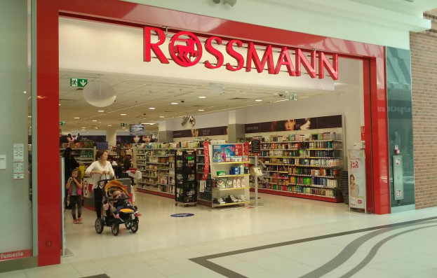Ein Rossmann-Laden in einem Einkaufszentrum mit Deckenbeleuchtung, Schildern, Menschen und Regalen mit Produkten.