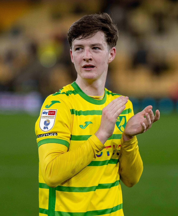 Ein junger Mann in einem gelb-grünen T-Shirt klatscht in den Händen, während er auf einem Fußballfeld steht und einen Torerfolg feiert, mit einem unscharfen Hintergrund.