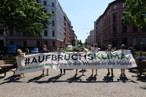 Eine Gruppe von Menschen in Masken, die ein Banner mit der Aufschrift 'Aufbruchsklima' während einer Klimaprotest in Berlin, Deutschland halten, mit sichtbaren städtischen Elementen im Hintergrund.