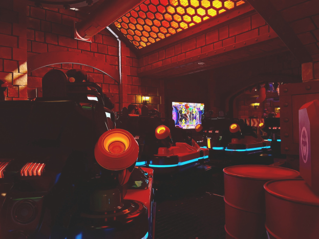 Ein hell erleuchteter Raum voller verschiedener Arcade-Videospielautomaten, Bildschirme und Gegenstände, einschließlich einer sichtbaren Röhre und Deckenbeleuchtung.
