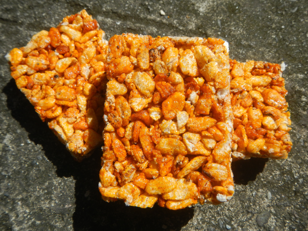 Nahaufnahme eines goldbraunen, knusprigen Snacks mit überlappenden Stücken auf einer flachen Oberfläche.