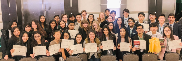 Gruppe von Menschen mit Urkunden, die in einem Raum mit Stühlen und einer Wand im Hintergrund für ein Foto posieren, wahrscheinlich feiern sie eine Abschlusszeremonie für das akademische Jahr 2019-2020.