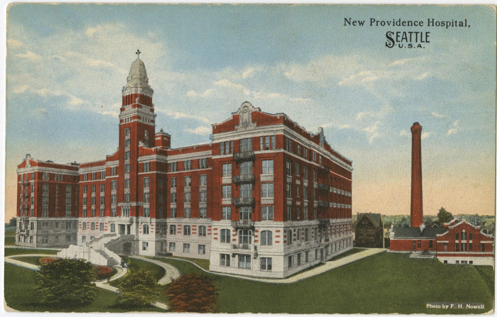 Eine Postkarte zeigt das New Providence Hospital in Seattle, Washington, mit seinem großen Gebäude, Treppen, Geländern, Bäumen, Gras und einem bewölkten Himmel, mit Text auf der Karte.