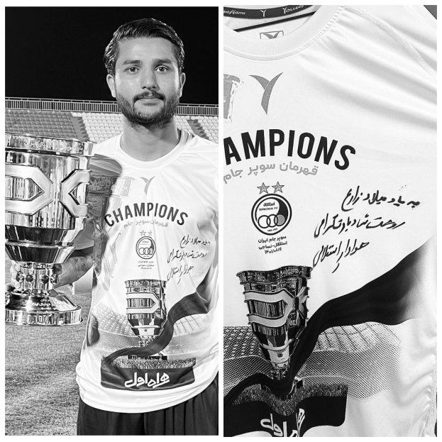 Ein Mann in einem weißen "Champions"-T-Shirt hält einen Pokal, während er in einem Stadion steht.