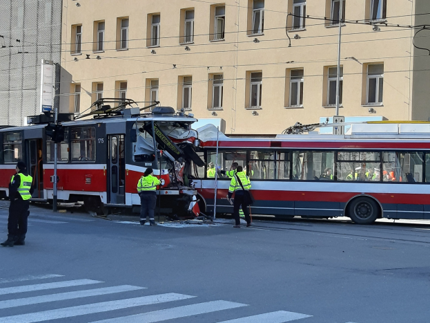 Rote und weiße Straßenbahn in einen Straßenrandunfall mit einigen Menschen in der Nähe und einem Gebäude im Hintergrund verwickelt.