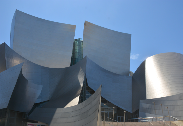 Die ARTIST Concert Hall in Los Angeles, ein modernes Gebäude mit Glaswänden, Treppen mit Geländern, die zum Eingang führen, umgeben von Laternenmasten, mit einer Tafel mit Text im Vordergrund und einem bewölkten Himmel im Hintergrund.