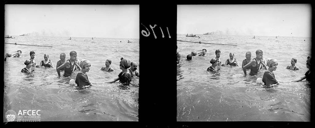 Ein Schwarz-Weiß-Foto einer Gruppe von Menschen, die in ruhigem, klarem Wasser bei einem Wettbewerb schwimmen, mit Booten im Hintergrund und Text in der linken unteren Ecke.