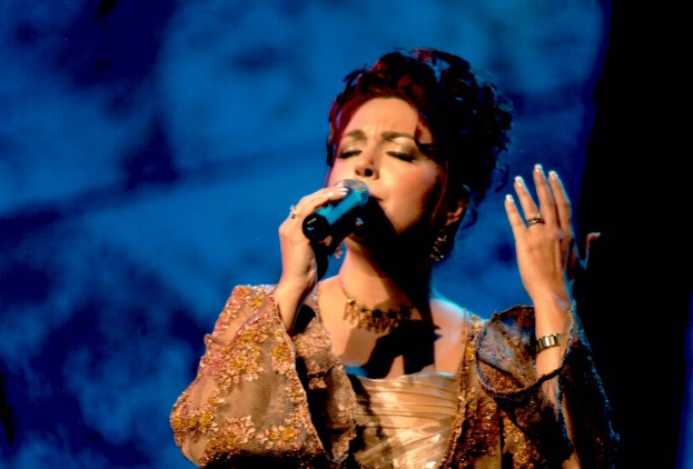 Frau in goldenem Kleid singt auf der Bühne der Eurovision Song Contest mit blauem und schwarzem Hintergrund.