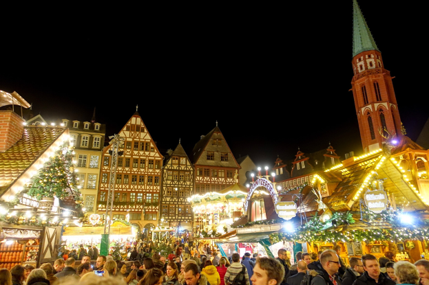 Ein geschäftiges Weihnachtsmarkt in Nürnberg, Deutschland mit Menschen um dekorierte Stände, festliche Lichter, Gebäude mit Fenstern, ein Uhrenturm und einen dunklen Himmel.