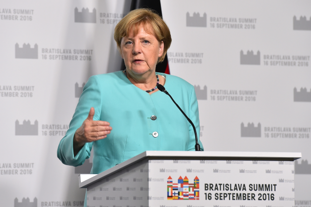 Bundeskanzlerin Angela Merkel hält eine Rede auf dem Bratislava-Gipfel, trägt ein blaues Kleid und steht vor einem Podium mit zwei Mikrofonen, im Hintergrund eine Fahne und ein Banner.