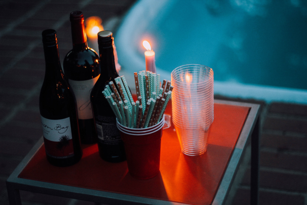 Ein Tisch am Swimmingpool mit zwei Weinflaschen, einer Kerze, Gläsern und Strohhalmen, der eine entspannte Nacht im Freien vermuten lässt.