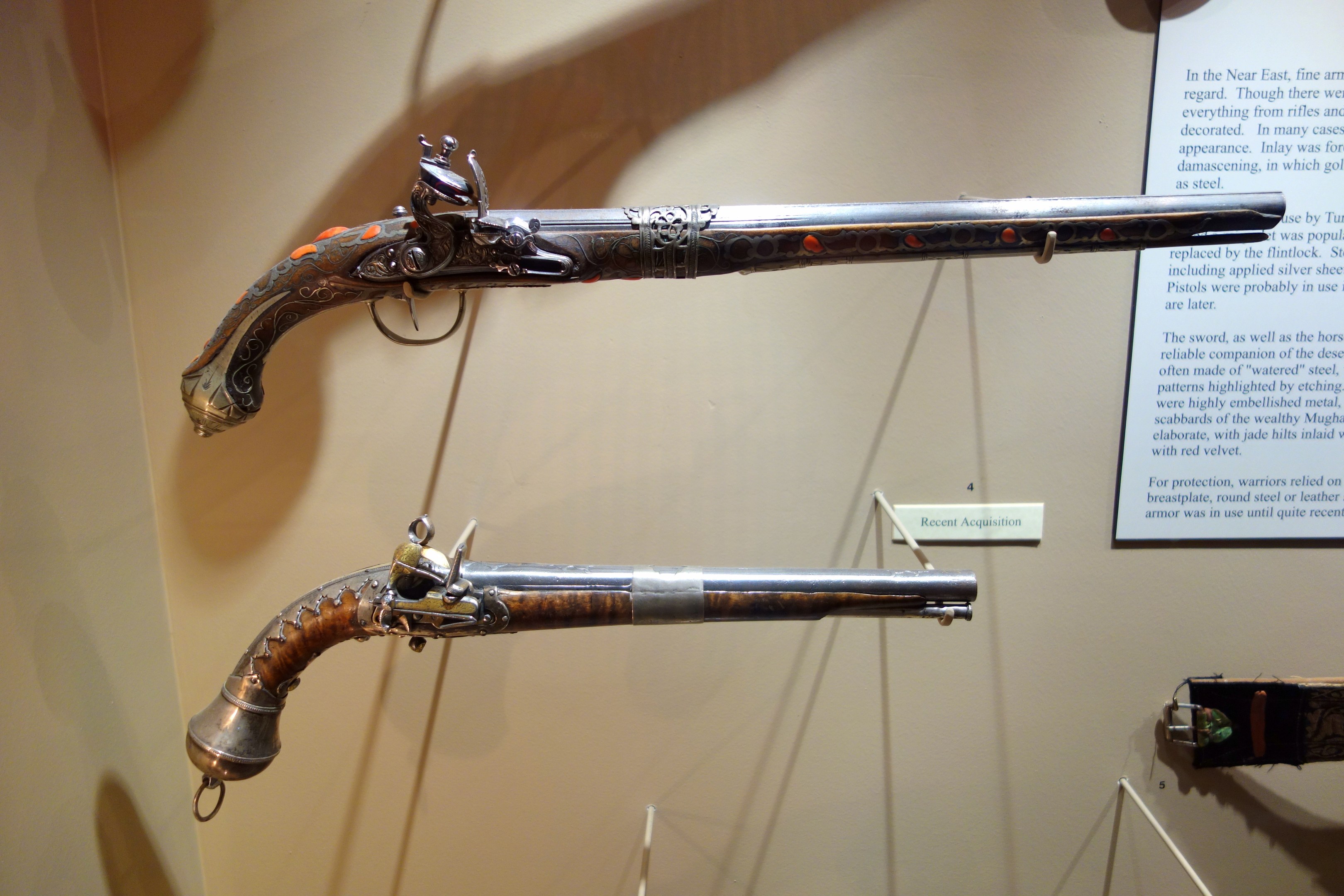 Zwei Flintenlockpistolen auf einem Museumsregal mit einer Texttafel im Hintergrund.