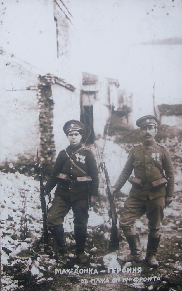 Zwei Männer in Militäruniformen stehen nebeneinander und halten Gewehre, im Hintergrund sind Gebäude und Steine zu sehen; Text unten lautet "Sergei Voloshin und sein Bruder Nikolai".
