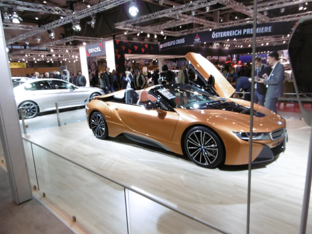 Ein elegantes schwarzes BMW i8 Cabrio mit Chromakzenten auf der Frankfurt Motor Show umgeben von formell gekleideten G├Ąsten.