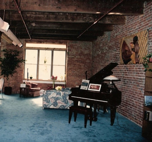 Ein Klavier mit zwei Notizbüchern darauf, eine Glasmalerei und ein Fenster im Hintergrund, mit einem kunstvoll gestalteten Dach.