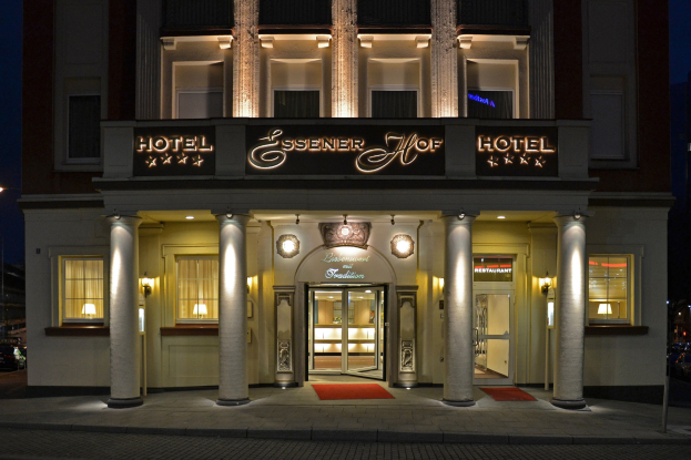 Das Essenerhof Hotel in Berlin, Deutschland, ein mehrstöckiges Gebäude mit Fenstern, Türen, Säulen, Lampen und einem Namensschild, mit einer Straße davor und Fahrzeugen auf der rechten Seite, unter einem sichtbaren Himmel.