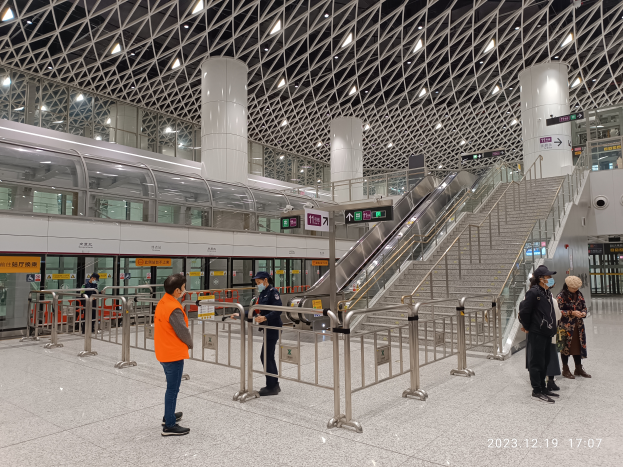 Eine Gruppe von Menschen, die in einem Flughafen-Terminal mit einer Rolltreppe, Gelöndern, Tafeln mit Text, Pfeilern, Deckenlampen und einem Zug auf der linken Seite steht, mit einem Wasserzeichen, das den Terminal aufgrund der Coronavirus-Pandemie als geschlossen kennzeichnet.