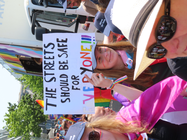 Eine Gruppe von Menschen steht vor einem Lkw und hält ein Schild mit der Aufschrift "Die Straßen sollten sicher sein". Einige tragen Mützen und Schutzbrillen, andere halten Schilder. Im Hintergrund sind Bäume, Gebäude und ein klarer blauer Himmel zu sehen.
