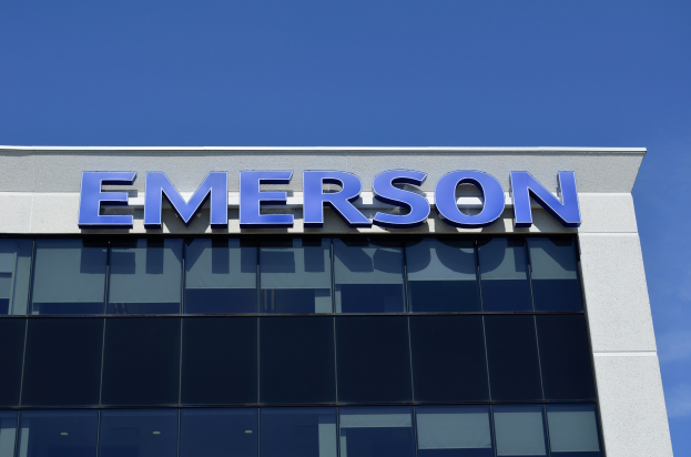 Emerson-Logo an der Seite eines Gebäudes mit dem Text "Emerson investiert 1,5 Milliarden US-Dollar in den USA" vor einem klaren blauen Himmel.