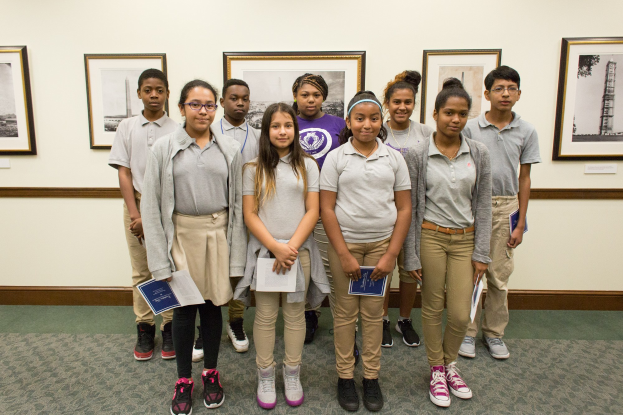 Eine Gruppe junger Schüler vor einer Wand mit Fotorahmen, jeder hält Bücher in der Hand.