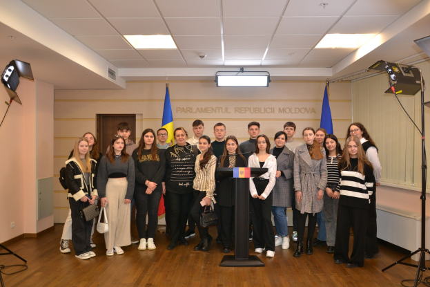 Gruppe von Menschen vor einem Podium mit einem Mikrofon beim Moldova Jugendkongress 2018, umgeben von Fahnen, einer Wand mit Text, einer Tür, Deckenleuchten und Scheinwerferstativen.